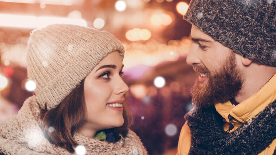 Junges Paar auf dem Weihnachtsmarkt mit Thermobechern in der Hand