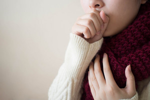 Woman coughing into her closed fist, holding her other hand to her throat