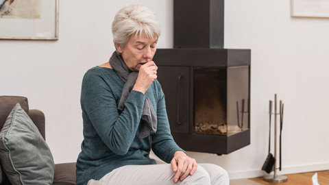 Eldery woman sitting on the couch in the living room coughing
