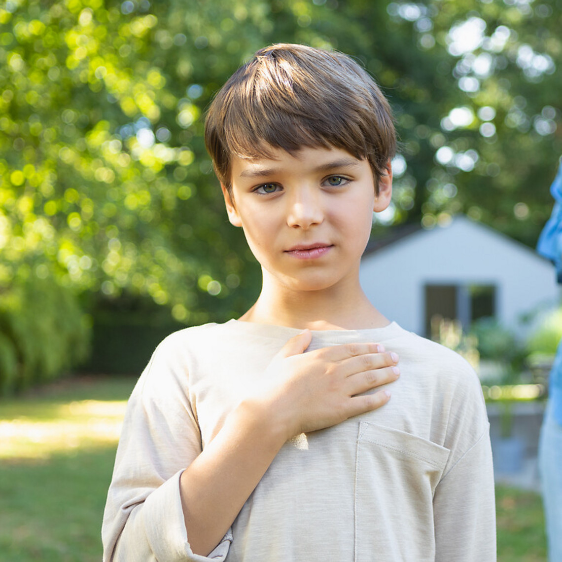 Junge hält sich die Hand auf die Brust, Mutter hält im Hintergrund Asthmaspray und VORTEX Inhalierhilfe bereit