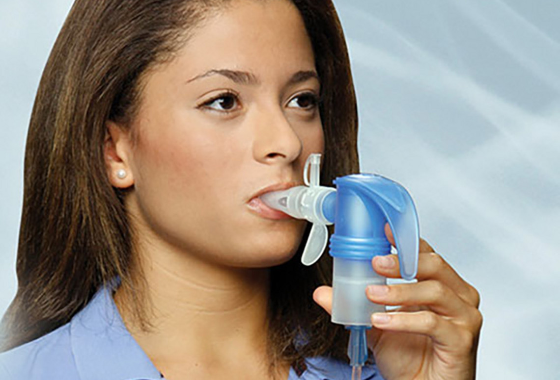 Person using a nebulizer to inhale medication mist for respiratory treatment in a clean clinical setting.
