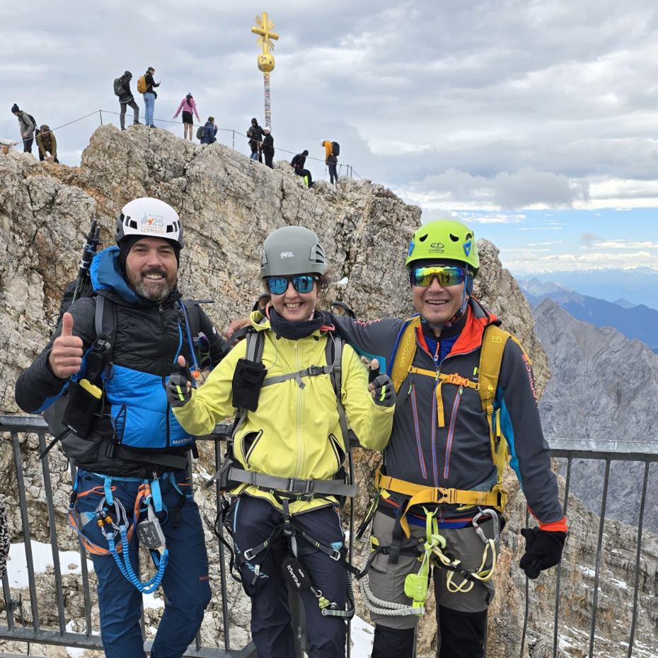 Zwei Männer und eine Frau posieren vor dem Gipfelkreuz der Zugspitze