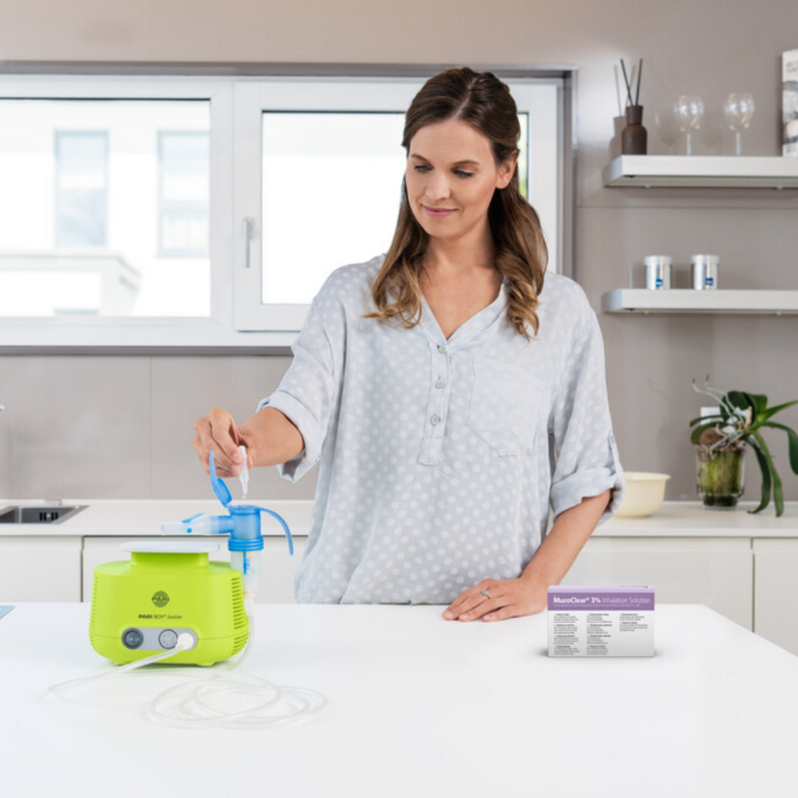 Newborn has a sniffle: Inhalation therapy with hypertonic saline solution Young woman stands at the table in the kitchen and fills hypertonic saline solution into the PARI BOY Junior inhalation device