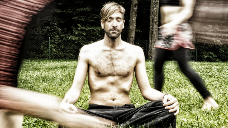 Mann sitzt im Schneidersitz mit geschlossenen Augen entspannt auf der Wiese