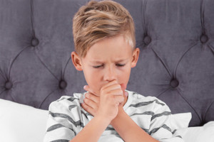 Boy sits in bed and holds his fist to his mouth