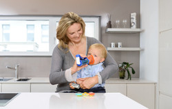 Mutter hält Baby im Arm mit Asthmaspray inkl. Spacer und Maske in der Küche