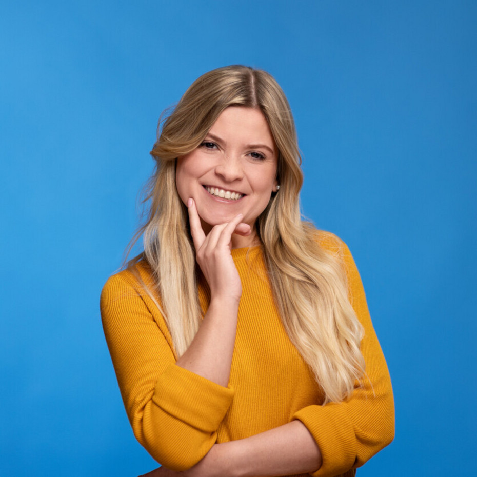 Half close-up of young smiling woman against a blue background, one hand on her chin