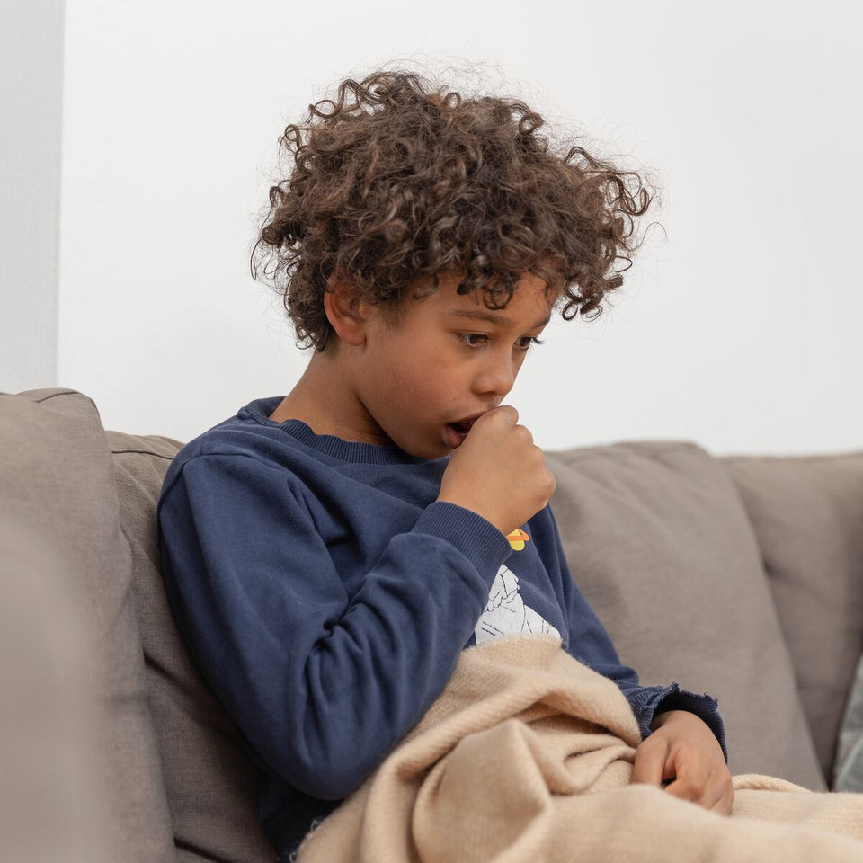 Bronchial hyperreactivity: What can you do if your bronchial tubes are hyperreactive? Junge sitzt auf der Couch mit einer Decke, er hustet und hält sich eine Faust vor den Mund