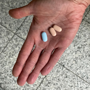 Close-up of an outstretched hand with a blue and two red tablets in the palm of the hand