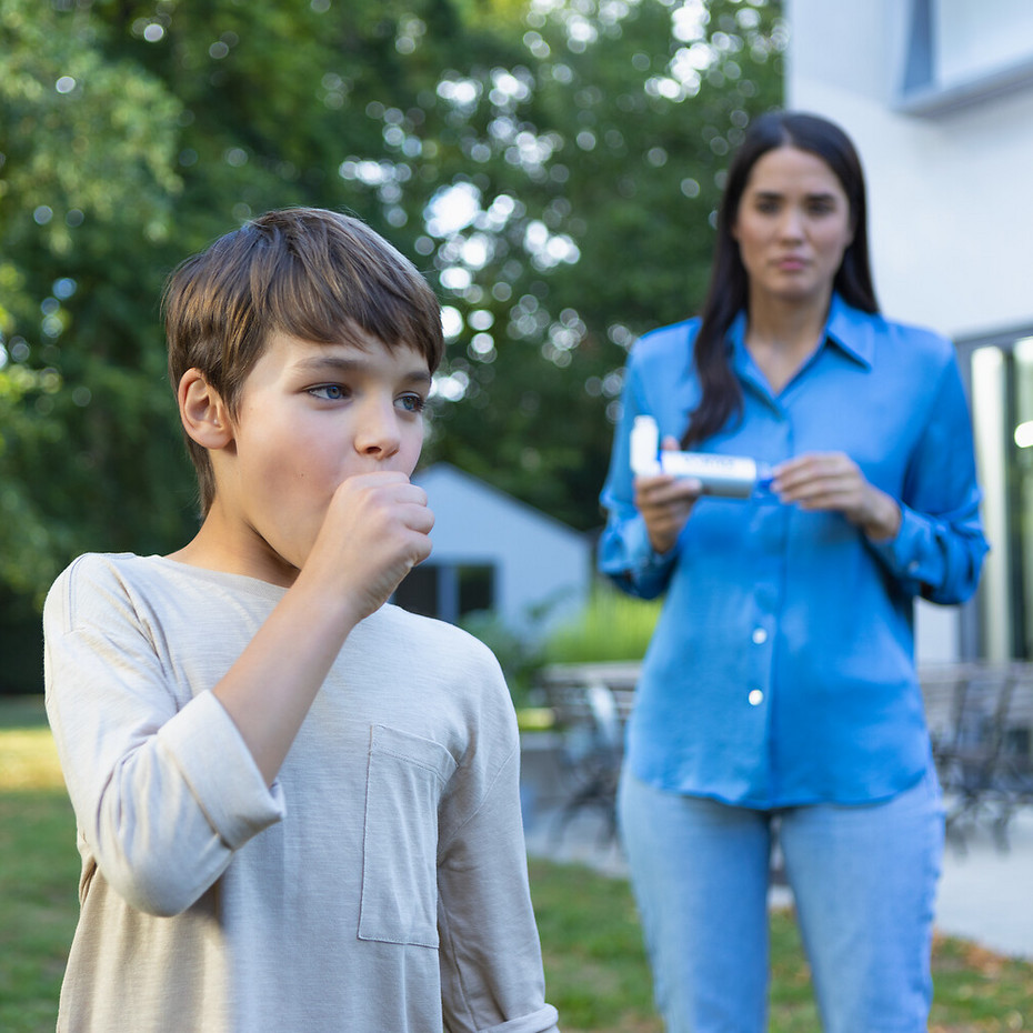 Boy coughing, mother in the background bringing asthma spray and VORTEX spacer