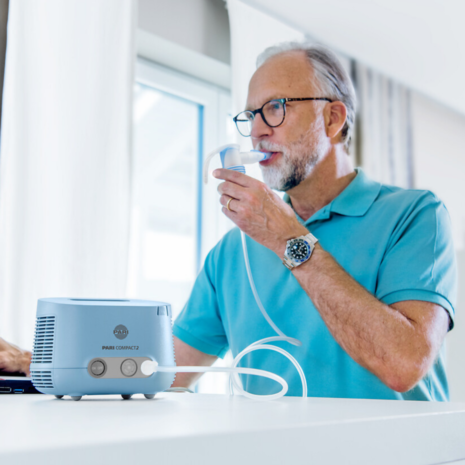 Älterer Mann sitzt an Tisch und inhaliert mit dem PARI COMPACT2
