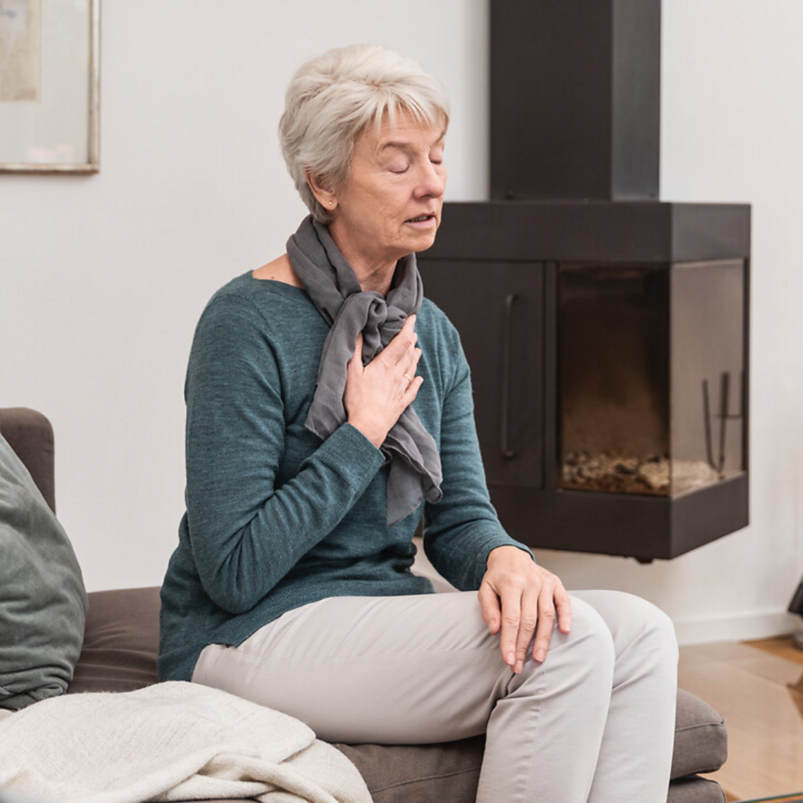 Old lady sitting on the sofa, holding one hand on her chest