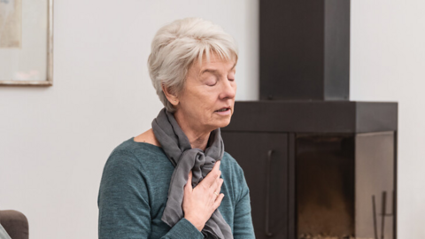 Old lady sitting on the sofa, holding one hand on her chest