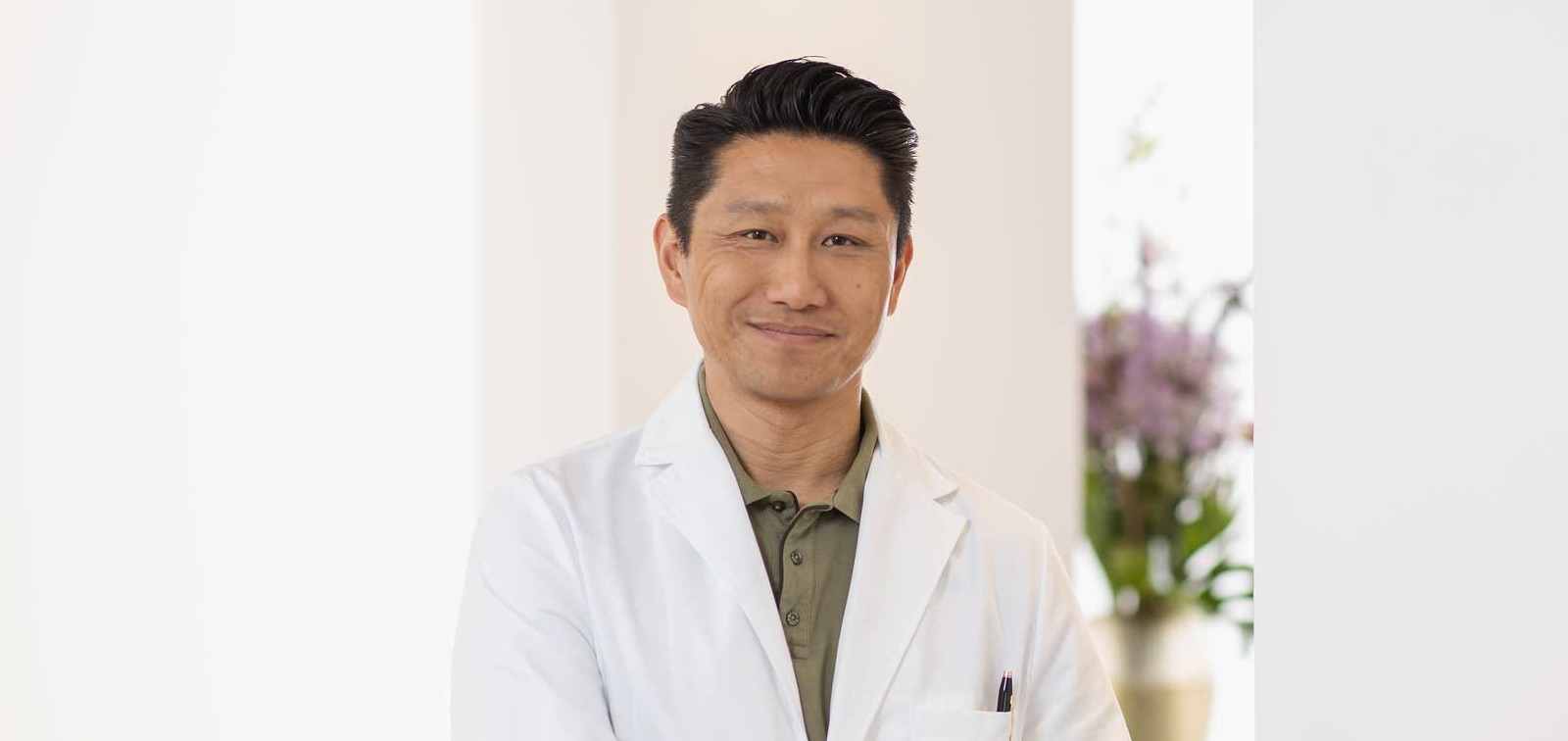 Männlicher Arzt mit weißem Kittel lehnt an einer Theke.