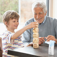 A child is stacking wooden blocks at a table; another person is sitting next to him; the PARI BOY Go inhaler is in the foreground.
