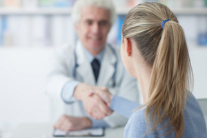 Elderly doctor shakes hands with young patient across desk