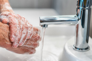 Eingeseifte Hände vor einem laufenden Wasserhahn