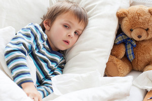 Small child lying ill in bed, teddy bear sitting next to the pillow