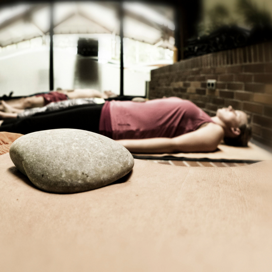 Junge Frau liegt entspannt auf Yogamatte, einen flachen Stein auf dem Bauch