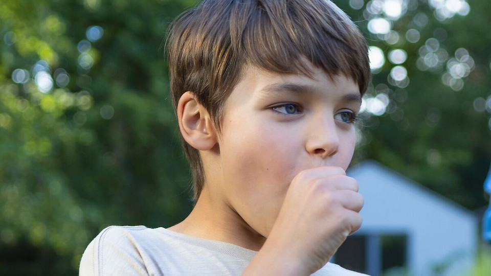 Young boy is coughing into his fist in the garden