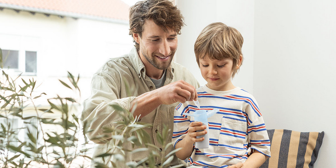 Kind hält einen tragbaren PARI BOY Go Kind hält einen tragbaren PARI BOY Go, während der Vater den Vernebler gemeinsam mit seinem Sohn befüllt.