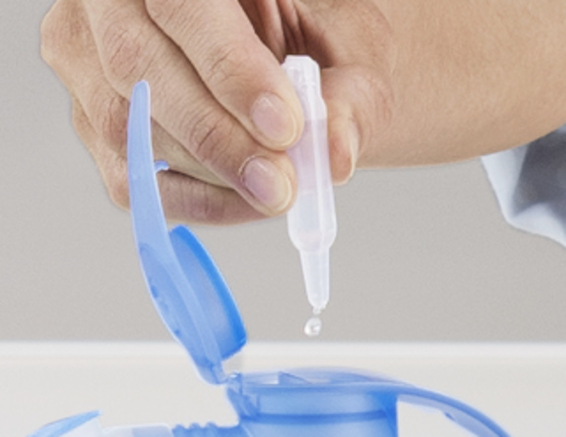 Inhalation for your health Hand holding a small ampoule and dripping saline solution into the open chamber of a blue nebuliser.