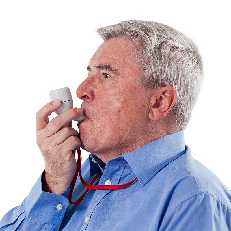 Um homem mais velho segura um dispositivo de terapia respiratória com fita vermelha e mantém o aparelho diante da boca.