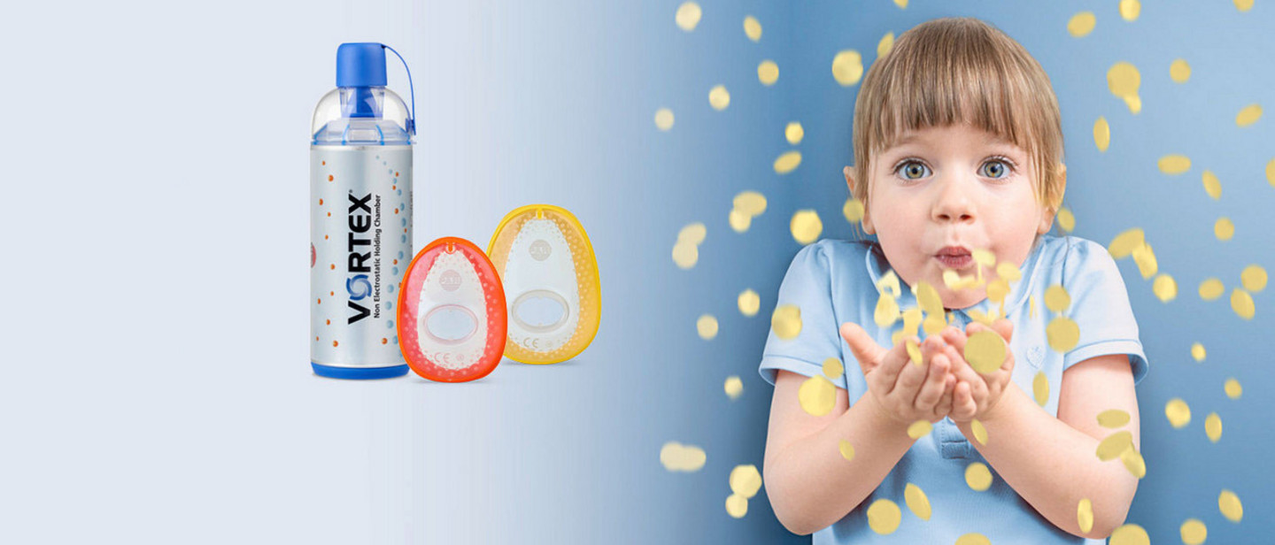 Ein Kind bläst goldenen Flitter aus ihren Händen der sich im Raum verteilt. Links daneben steht eine VORTEX Inhalierhilfe, daneben liegen eine Baby- und Kinder-Maske.