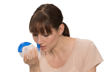 Frau hält Nasendusche an ihr Nasenloch mit leicht vornüber gebeugtem Oberkörper
