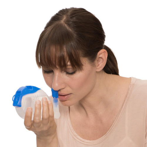 Frau hält Nasendusche an ihr Nasenloch mit leicht vornüber gebeugtem Oberkörper