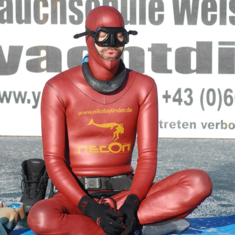 Taucher sitzt im Schneidersitz vor Eisloch