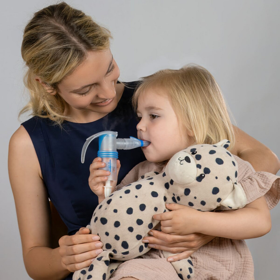 Calming irritated bronchial tubes: Inhaling saline solution A girl sits on her mother's lap, holding a cuddly toy in one hand and a nebuliser, which she uses to inhale, in the other