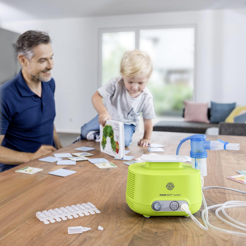 Vater und Sohn spielen auf einem Tisch. Im Vordergrund steht ein PARI BOY Junior Inhaliergerät.