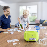 Vater und Sohn spielen auf einem Tisch. Im Vordergrund steht ein PARI BOY Junior Inhaliergerät.