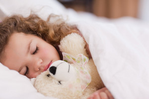 Kleines Mädchen liegt mit Teddybär schlafend im Bett