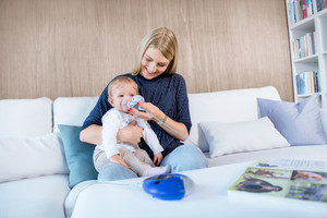Mutter hilft ihrem Baby auf der Couch sitzend beim Inhalieren