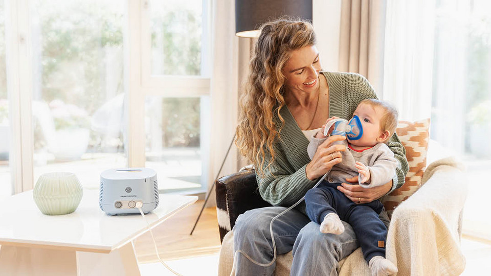 Young mother helping baby to inhale with a nebuliser