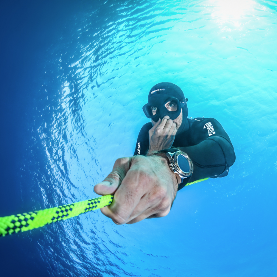 Taucher von oben fotografiert, er hält sich die Nase zu und hat eine Hand an einem Seil