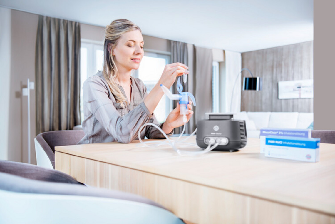 A woman sits at a table filling the PARI SINUS2 with inhalation solution