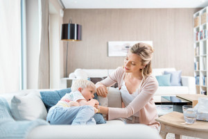 Junge liegt krank auf der Couch, Mutter tröstet ihn