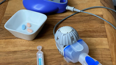Wirklich nicht mehr inhalieren unter der Therapie mit Triple-CFTR-Modulatoren? Erfahrungen einer Mukoviszidose-Patientin Inhalationsgerät mit Controller, Inhalationslösung und Schale mit Tabletten auf einem Tischchen