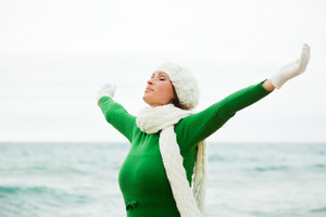 Young woman with beanie and scarf and arms outstretched breathing sea air