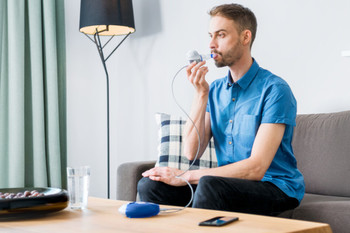 Mann sitzt auf dem Sofa und inhaliert mit einem Inhaliergerät