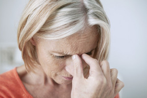 Ältere Frau in Nahaufnahme hält sich die Nasenwurzel und scheint Schmerzen zu haben