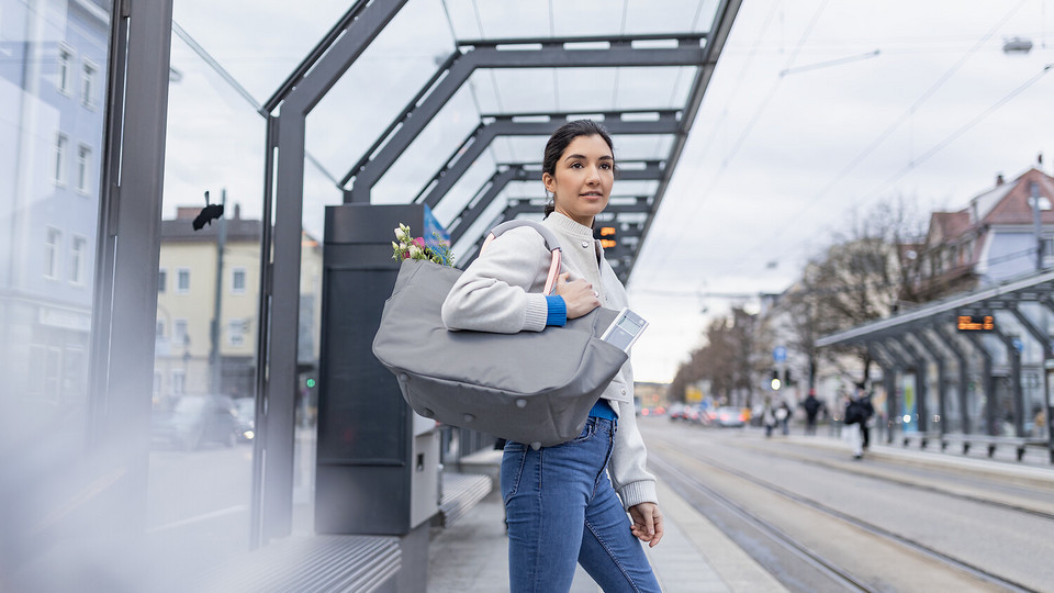 Junge Frau mit CF steht an Tram-Haltestelle