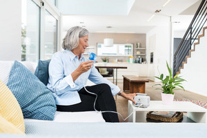 Elderly woman inhaling at living room table with PARI BOY