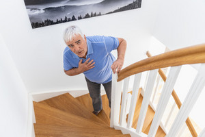 Elderly man standing on stairs with his hand on his lungs, finding it difficult to breathe