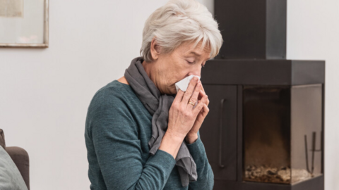 Schleim bei COPD und Bronchiektasen: Interview mit Prof. Dr. Fischer Ältere Frau sitzt auf der Couch im Wohnzimmer und putzt sich die Nase