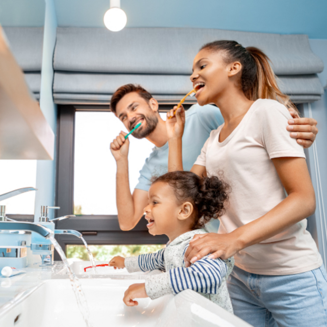 Nebenwirkungen von Kortisonsprays bei Asthma reduzieren: danach Zähne putzen Mutter, Vater und Kind stehen im Bad vor dem Waschbecken und putzen Zähne