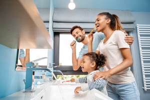 Mother, father and child standing in bathroom in front of mirror brushing teeth